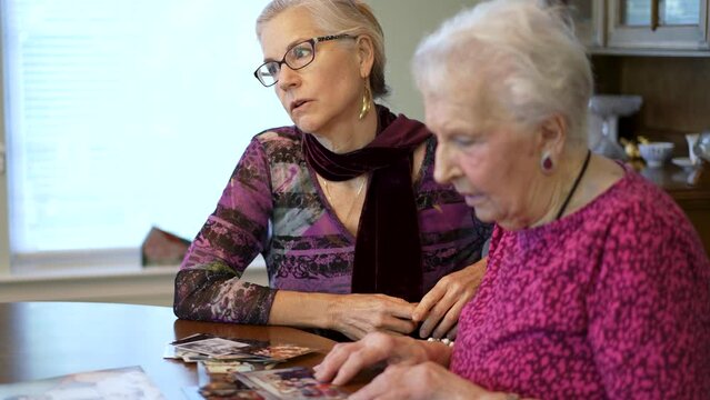 Senior elderly woman looking at old photos and remembering memories with daughter at the dining room table.
