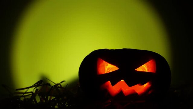 Halloween pumpkin glowing inside in the dark. Shadow of scary pumpkin behind it. Close-up in 4K
