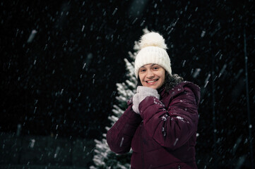 Portrait of a charming dark-haired multi-ethnic woman in warm clothes, white wool hat and mittens, smiling a beautiful toothy smile looking at the camera, standing in the snow covered nature.