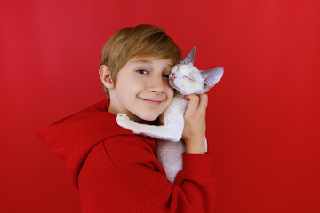 close-up of a boy who holds a small white cat leaned against him and gently hugs the cat
