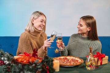 Two girls are sitting on the sofa and relaxing at New Year's parties. Two girls celebrate the New Year with glasses of champagne.