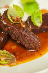 Delicious veal cheeks in red sauce  closeup on a white plate on white background