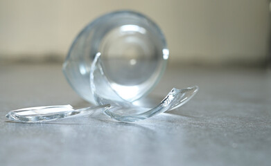 Empty drinking glass falling on the gray tile floor and cracked to small shattered and sharp. Closeup broken beverage glass crash, accident in home