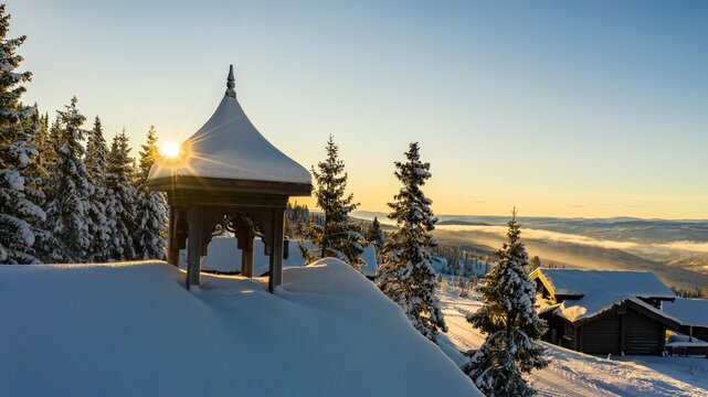 Beautiful Shot Of The Sun Shining Over A House Roof Covered In Snow On A Snowy Mountain