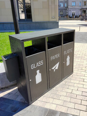 Sorting garbage bins on the street, which are divided into GLASS, PAPER and PLASTIC with the corresponding logo