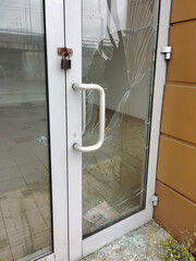 The glass of a store door broken by thieves or vandals with a padlock hanging from it