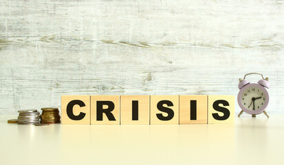 Six wooden cubes with letters are on the table next to the coins. The word is CRISIS. On a gray background.