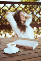 Cup of coffee and book at table and relaxed woman in background