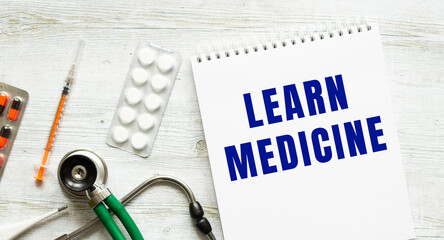 LEARN MEDICINE is written in a notebook on a white table next to pills and a stethoscope.