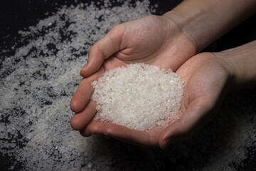 Hands holding coarse rock salt on a black background. Large salt crystals