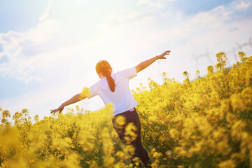 girl raising her hands on sides. freedom, victory, and power. back view of a girl standing on a yellow blooming field. dream to take off and fly away