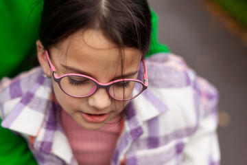 Beautiful little girl in glasses and a plaid shirt close-up on a blurred autumn background
