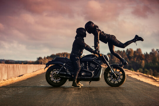 Happy couple with motorcycle at the evening kissing each other. Romantic scene with man and woman at the motorcycle 