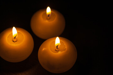 Burning bright golden candles on black background. Festive or mourning candles.
