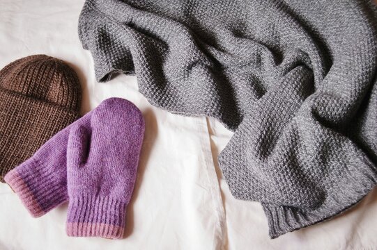 Winter clothes for women. Brown hat, purple gloves and gray woolen scarf. Flat lay photography knitted clothing