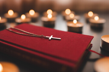 Silver christian cross on red paper bible book on table over burning candles close up