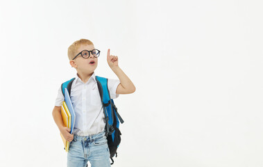 Back to school. Funny little boy from elementary school with a book, a backpack and glasses on a white background. Laughs merrily. Preparation for school. Concept of early development