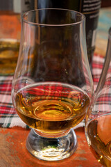 Tulip-shaped tasting glass with dram of Scotch single malt or blended whisky on wooden table with tartan