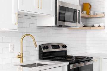A gold faucet detail shot in a white kitchen, subway tile backsplash, and stainless steel appliances.
