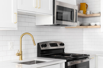 A gold faucet detail shot in a white kitchen, subway tile backsplash, and stainless steel...