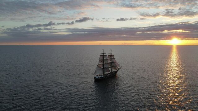 fast rotating aerial shot of a tall ship sailing into the sunset