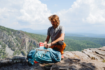 The guy packs a first aid kit in a backpack sitting on the mountain, a tourist collects equipment...