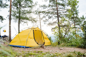 A yellow tent stands in the forest high in the mountains, tourist camping, a summer day in nature, a vacation in the forest, an open entrance.