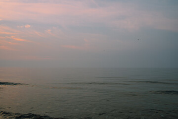 tranquil, quiet pink and blue smoky sunset over water with clouds	