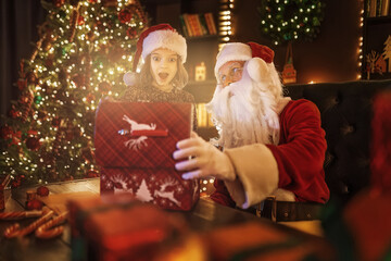 Santa Claus surprising little girl while open magical box near Christmas tree. New Year concept