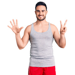 Young handsome man wearing swimwear and sleeveless t-shirt showing and pointing up with fingers number seven while smiling confident and happy.