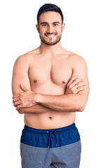 Young handsome man wearing swimwear happy face smiling with crossed arms looking at the camera. positive person.
