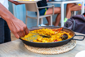 Mediterranean paella, seafood rice meal on the coast of Ibiza, waiter serving