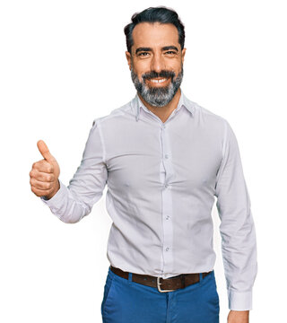 Middle aged man with beard wearing casual white shirt smiling happy and positive, thumb up doing excellent and approval sign