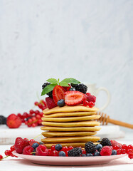 Stack of baked pancakes with fruits in a round plate on a white table