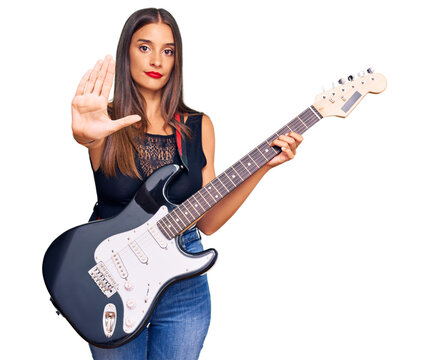 Young hispanic woman playing electric guitar with open hand doing stop sign with serious and confident expression, defense gesture - Powered by Adobe