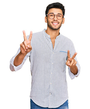 Young handsome man wearing casual clothes and glasses smiling looking to the camera showing fingers doing victory sign. number two.