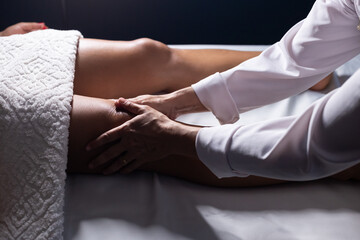 Massoterapeuta fazendo massagem no joelho de paciente deitada em maca.