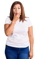 Fototapeta premium Middle age latin woman wearing casual white tshirt looking fascinated with disbelief, surprise and amazed expression with hands on chin