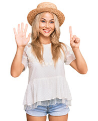 Obraz na płótnie Canvas Young blonde girl wearing summer hat showing and pointing up with fingers number six while smiling confident and happy.