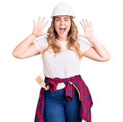 Young caucasian woman wearing security helmet showing and pointing up with fingers number ten while smiling confident and happy.