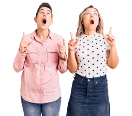 Couple of women wearing casual clothes amazed and surprised looking up and pointing with fingers and raised arms.