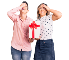Couple of women holding gift stressed and frustrated with hand on head, surprised and angry face