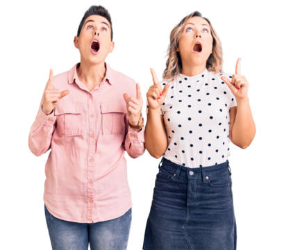 Couple of women wearing casual clothes amazed and surprised looking up and pointing with fingers and raised arms.