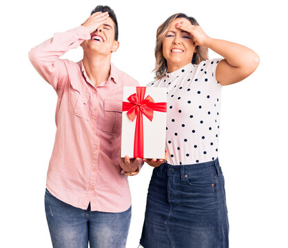 Couple of women holding gift stressed and frustrated with hand on head, surprised and angry face