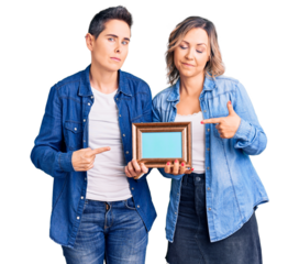 Couple of women holding empty frame pointing with hand finger to the side showing advertisement, serious and calm face