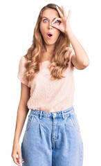 Fototapeta premium Young beautiful caucasian woman with blond hair wearing casual clothes doing ok gesture shocked with surprised face, eye looking through fingers. unbelieving expression.