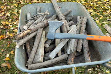 The chopped firewood lies in a garden cart and an axe for chopping wood lies on top.
