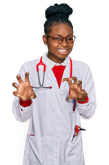 Young african american woman wearing doctor uniform and stethoscope smiling funny doing claw...