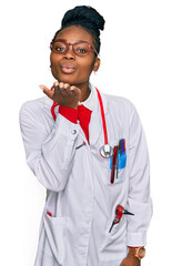 Young african american woman wearing doctor uniform and stethoscope looking at the camera blowing a kiss with hand on air being lovely and sexy. love expression.