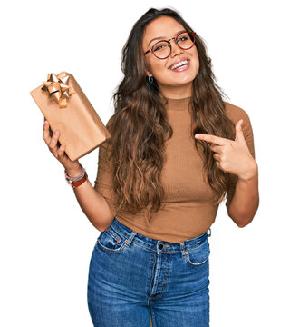 Young hispanic girl holding gift smiling happy pointing with hand and finger